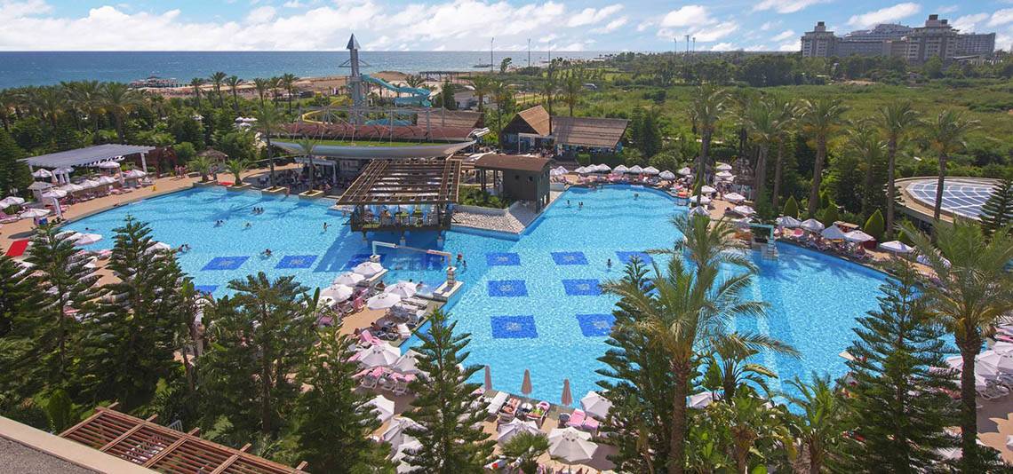 Luftaufnahme des Delphin Diva Premiere Pools mit Wasserrutsche, Sonnenschirmen und Hotel im Hintergrund.
