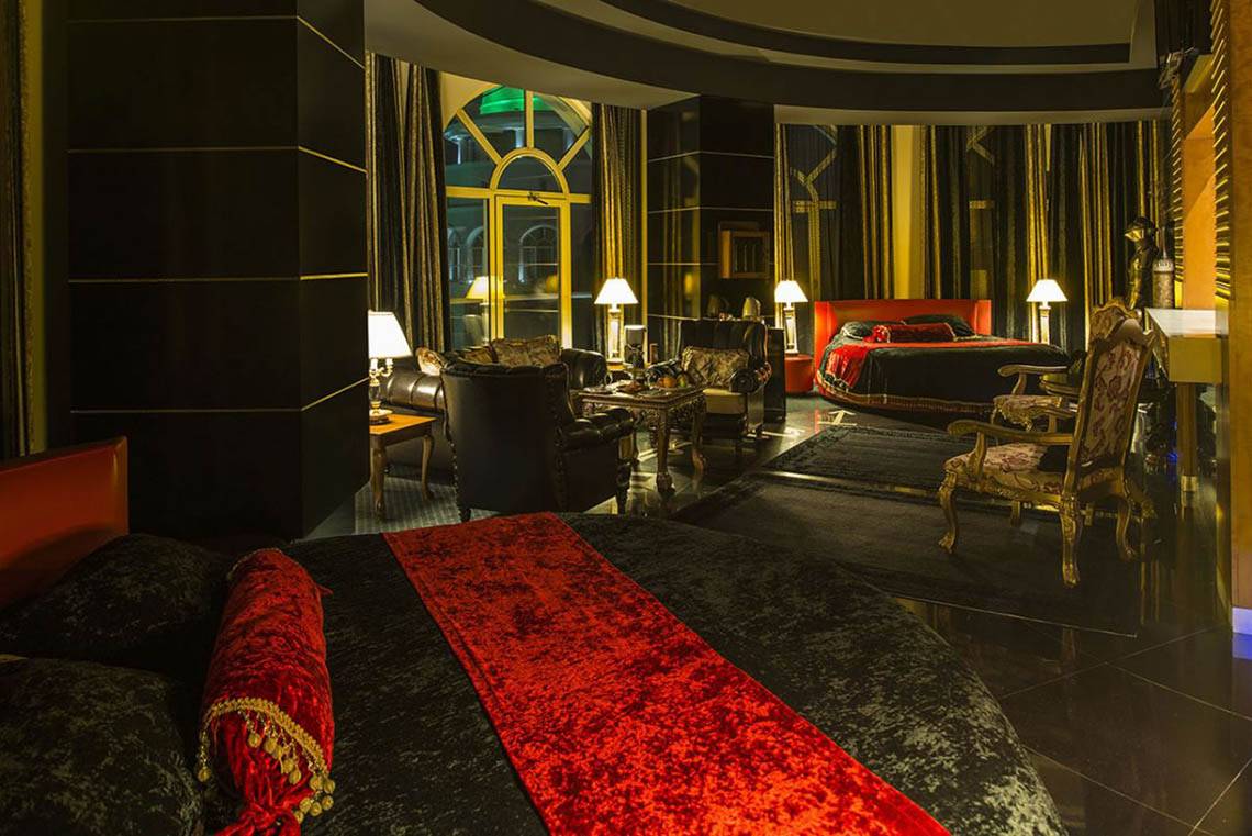 Innenansicht einer Hotelsuite im Delphin Diva Premiere mit rotem Bett, goldenen Stühlen und schwarzen Möbeln.