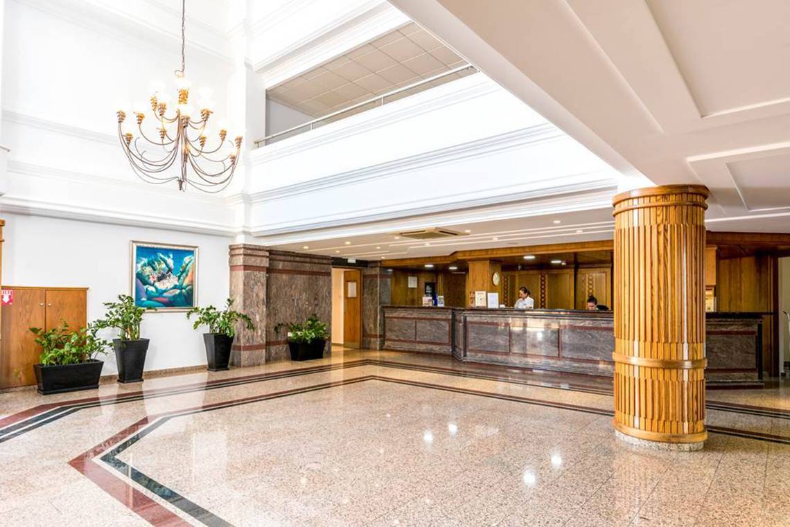 Eingangsbereich des Nissiana Hotels mit Rezeptionstresen, Kronleuchter und Pflanzen.