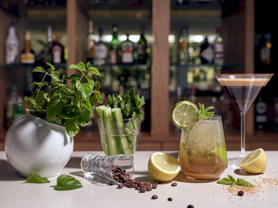 Cocktails auf einer Holztischplatte im Hotel Caravel mit Pflanzen, Zitronen und Kaffeebohnen.