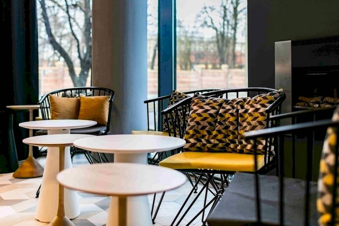 Loungebereich des NH Berlin Alexanderplatz Hotels mit modernen Möbeln und Blick auf Bäume.