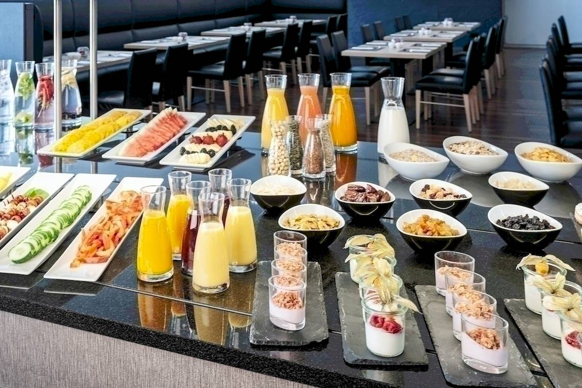 Buffet-Tisch im NH Berlin Alexanderplatz Hotel mit verschiedenen Speisen und Getränken.