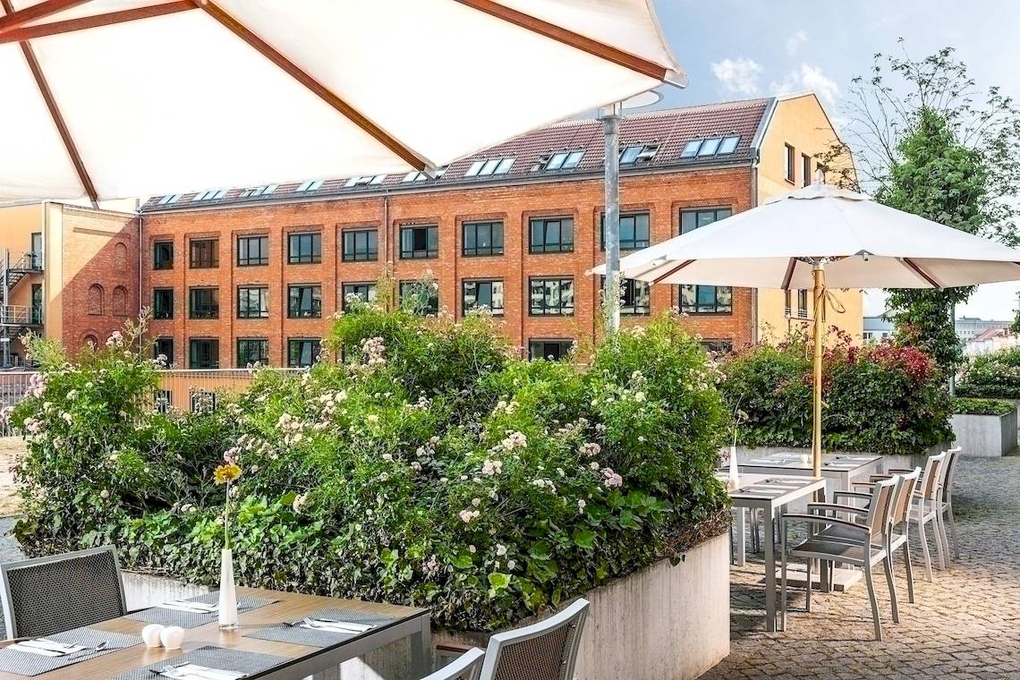 Außenbereich des NH Berlin Alexanderplatz Hotels mit Tischen und Stühlen unter Schirmen.