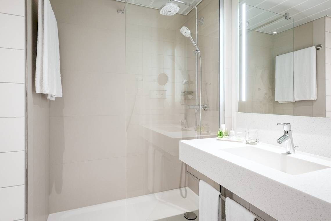 Badezimmer im NH Berlin Alexanderplatz Hotel mit Glasdusche und Waschbecken.