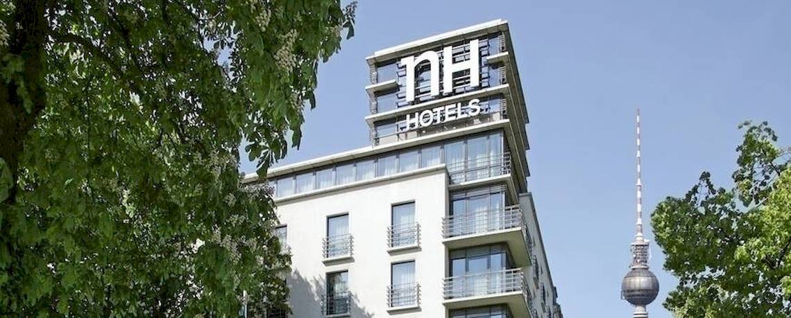 Außenansicht des NH Berlin Alexanderplatz Hotels mit grünen Bäumen und Berliner Fernsehturm.