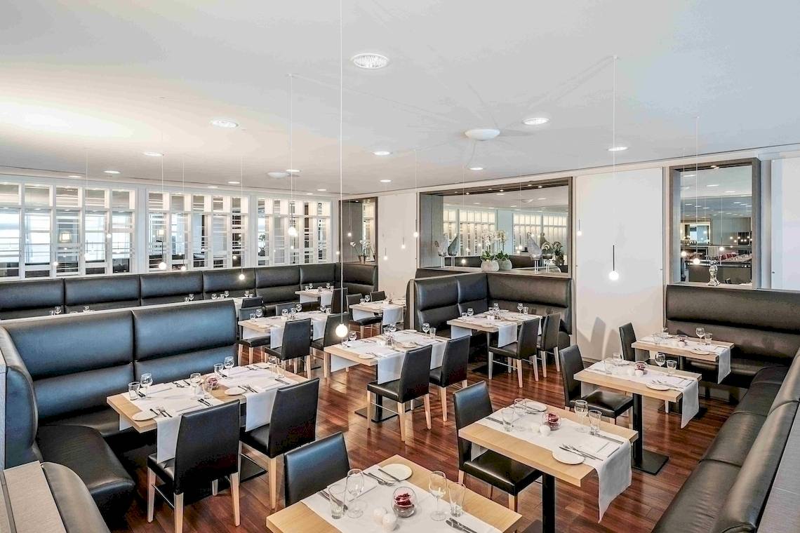 Innenansicht des Restaurants im NH Berlin Alexanderplatz Hotel mit gedeckten Tischen und Stühlen.