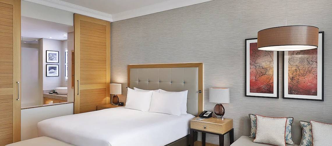 Hotelzimmer im Hilton Cabo Verde Sal Resort mit einem Bett, Nachttischen, Lampen und Gemälden an der Wand.