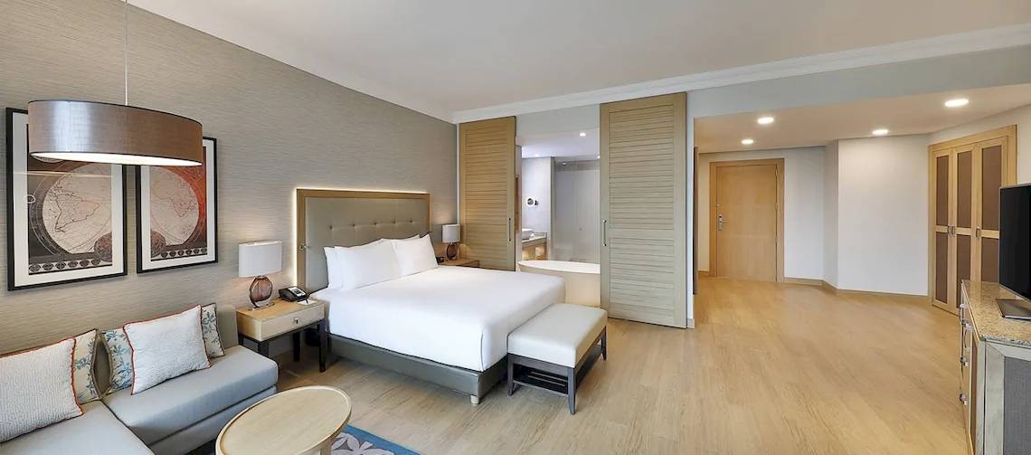 Inneneinrichtung der Suite im Hilton Cabo Verde Sal Resort mit einem großen Bett, Couch und Nachttisch.