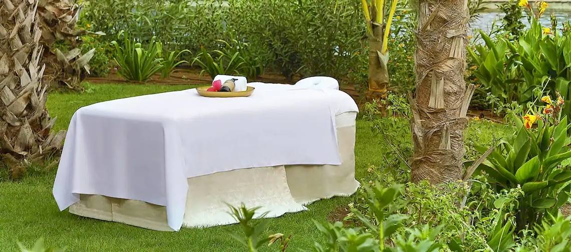 Massagetisch im Garten des Hilton Cabo Verde Sal Resort, mit weißem Tischtuch und Pflanzen im Hintergrund.