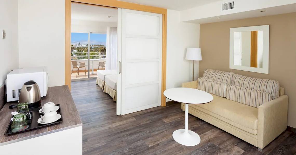 Innenansicht eines Zimmers im Sol Lanzarote All Inclusive Hotel mit einem kleinen Tisch, einer Couch und einem offenen Balkon.