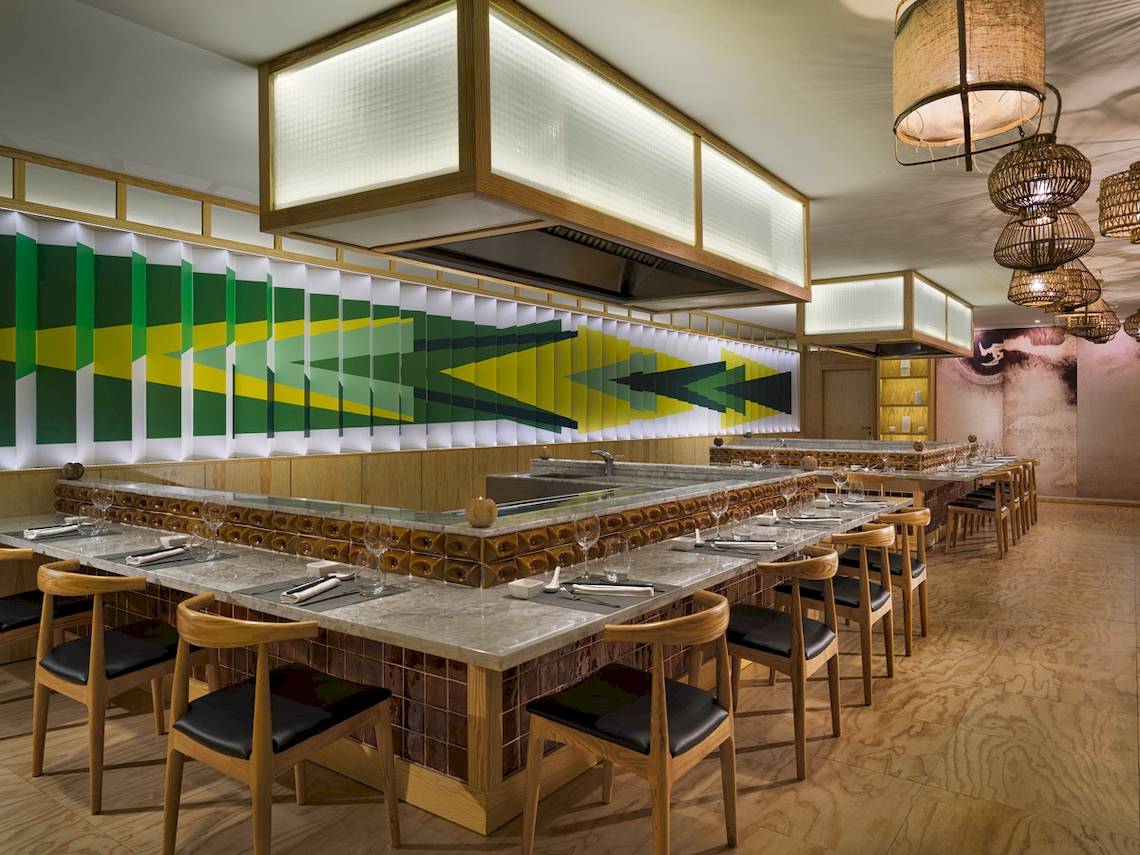 Innenansicht des Restaurants H10 Lanzarote Princess mit grünen und gelben Wandmustern, Holztischen und Stühlen.