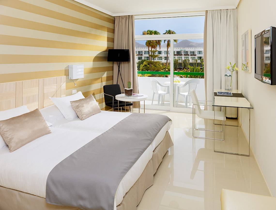 Innenansicht eines Zimmers im H10 Lanzarote Princess Hotel mit Bett, Schreibtisch und Balkon.