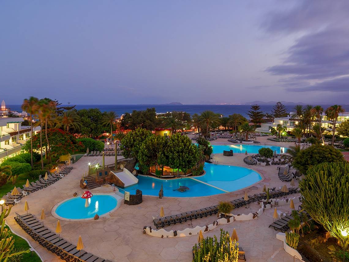 Abendausblick auf den Swimmingpool des H10 Lanzarote Princess Hotels mit Sonnenliegen und tropischen Pflanzen.