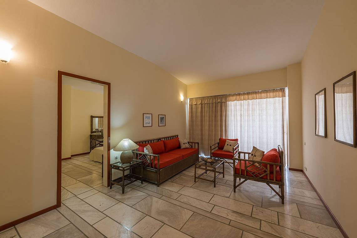 Wohnzimmer im Pavlina Beach Hotel mit rotem Sofa und Tisch, davor ein Nachttisch mit Lampe.