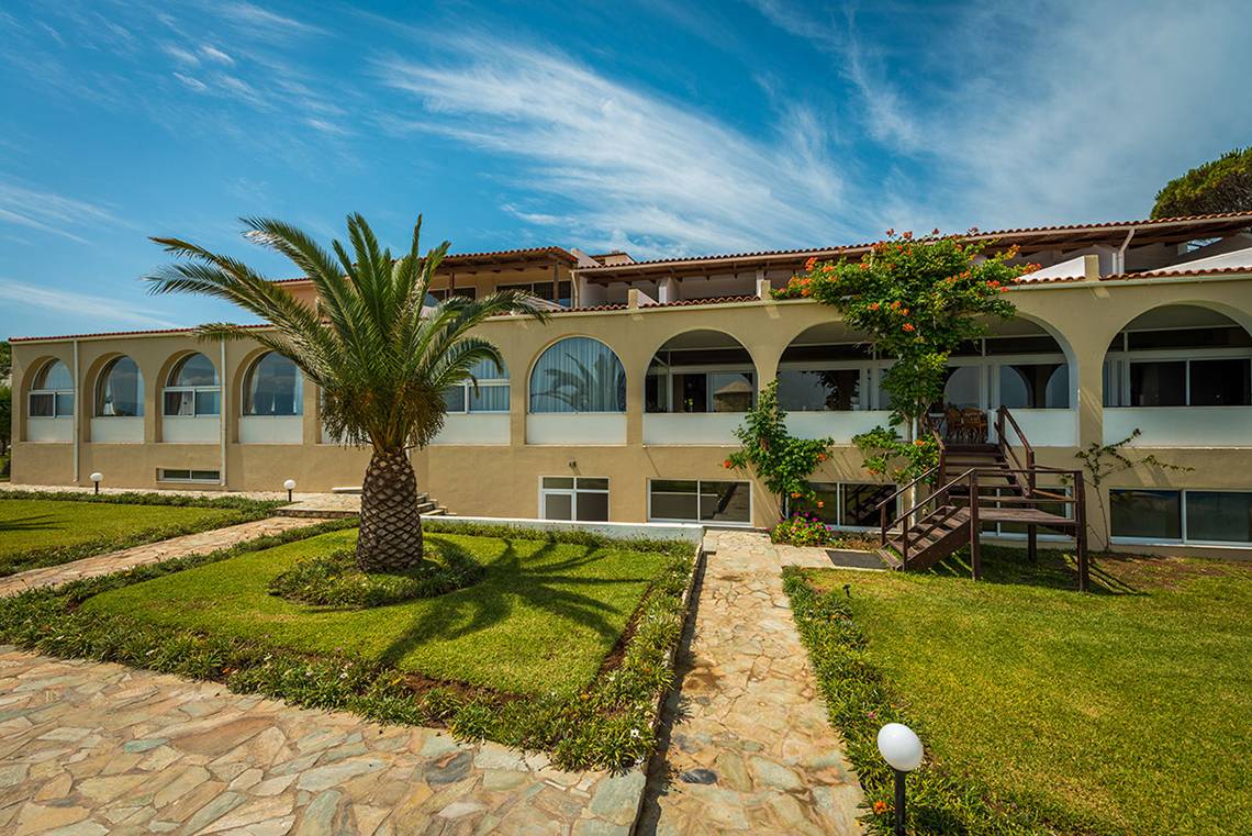 Außenansicht des Pavlina Beach Hotels mit gepflasterten Wegen, Palmbaum und Treppe.