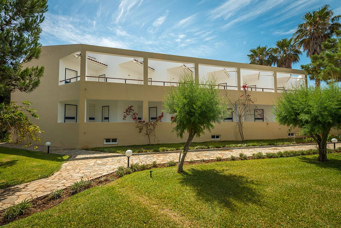 Außenansicht des Pavlina Beach Hotels mit mehreren Stockwerken, Balkonen und umliegender Grünfläche.