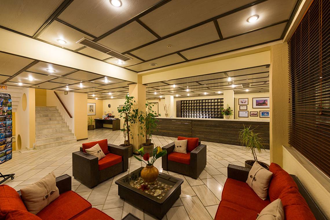 Lobby des Pavlina Beach Hotels mit roten Sofas, Tischen, Pflanzen und einer Rezeption.