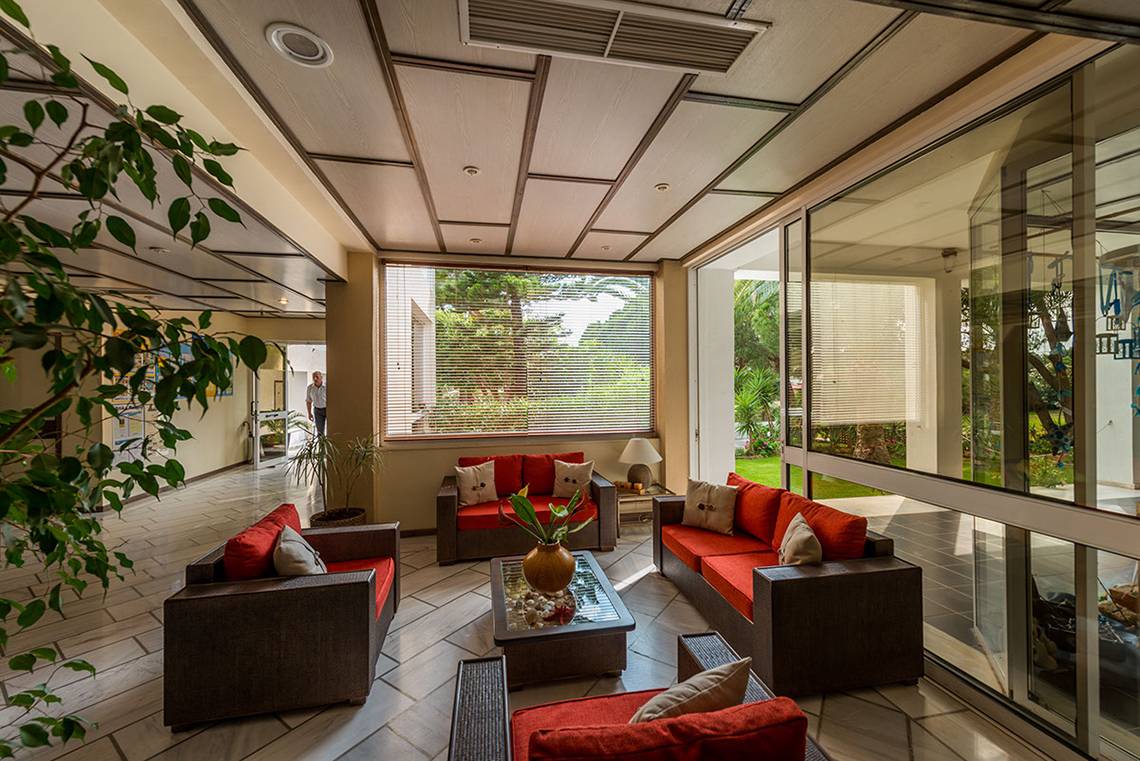 Lobby-Lounge im Pavlina Beach Hotel mit roten Sofas, Glaswänden und Pflanzen.