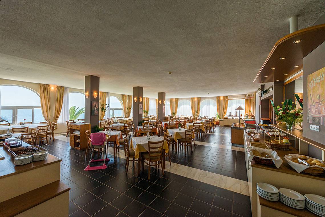 Innenansicht des Restaurants im Pavlina Beach Hotel mit Tischen, Stühlen und Meeresblick.