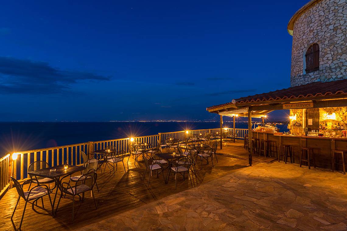Abendansicht der Pavlina Beach Bar mit Blick auf das Meer und beleuchteten Tischen und Stühlen.