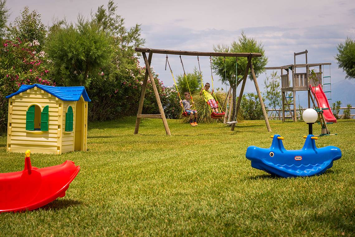 Kinderspielplatz im Pavlina Beach Hotel mit Schaukeln, Rutsche und Spielhaus.