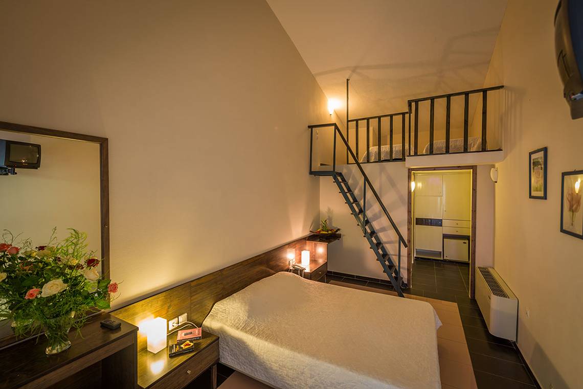 Innenansicht eines Zimmers im Pavlina Beach Hotel mit einem Doppelbett, Nachttisch, Spiegel, Blumenvase, und einem Aufgang zur oberen Etage.