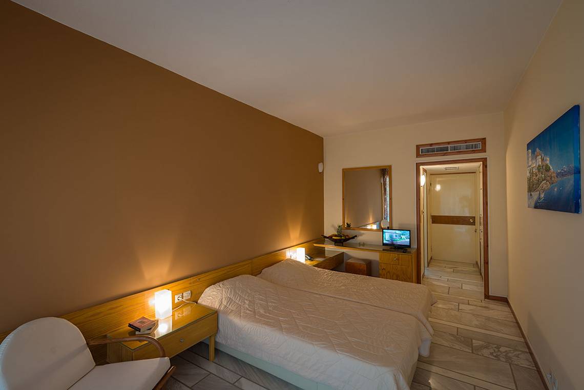 Doppelzimmer im Pavlina Beach Hotel mit zwei Betten, Fernseher, Tisch, Stuhl und Spiegel.