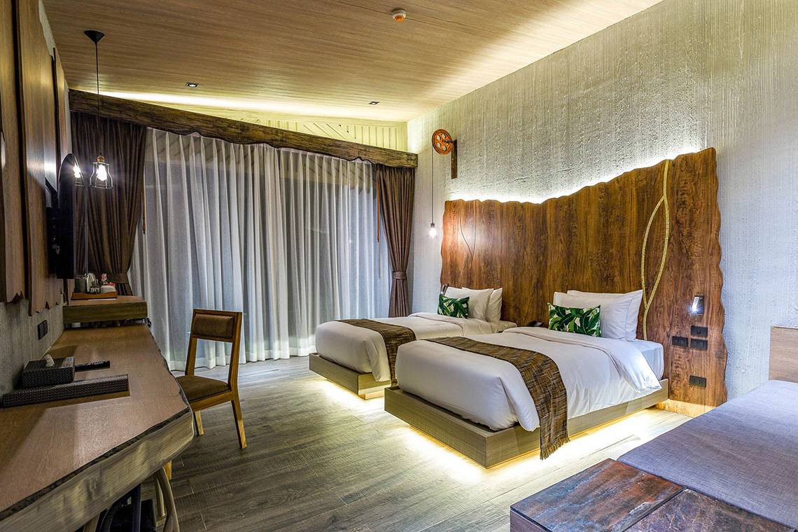 Doppelbettzimmer im Kalima Resort & Villas Khao Lak mit zwei Betten, Schreibtisch und modernen Holzelementen.