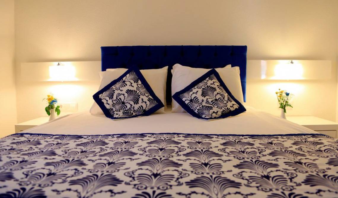 Bett im LABRANDA Ephesus Princess Hotel mit blau-weißem Design und Blumenvasen auf Nachttischen.