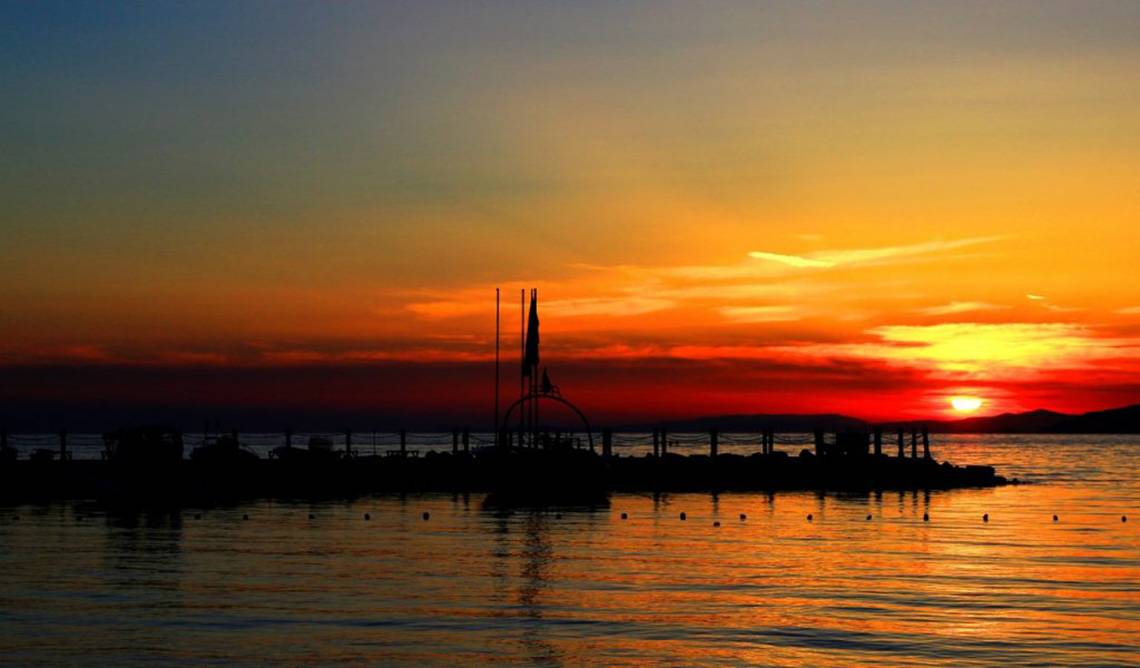 Sonnenuntergang am Meer mit einer Struktur im Wasser, die Schatten wirft.
