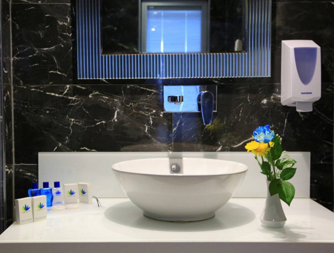 Ein Badezimmer im LABRANDA Ephesus Princess Hotel mit schwarzen Marmorfliesen, einem weißen Waschbecken und blauen Blumen in einer Vase.