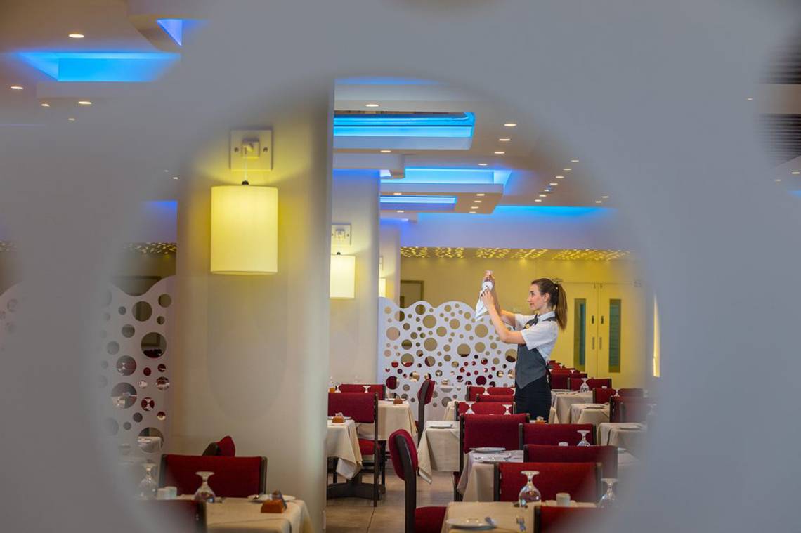 Mitarbeiterin im Cavo Maris Beach Hotel Restaurant, das eine weiße Wand und rote Stühle hat.