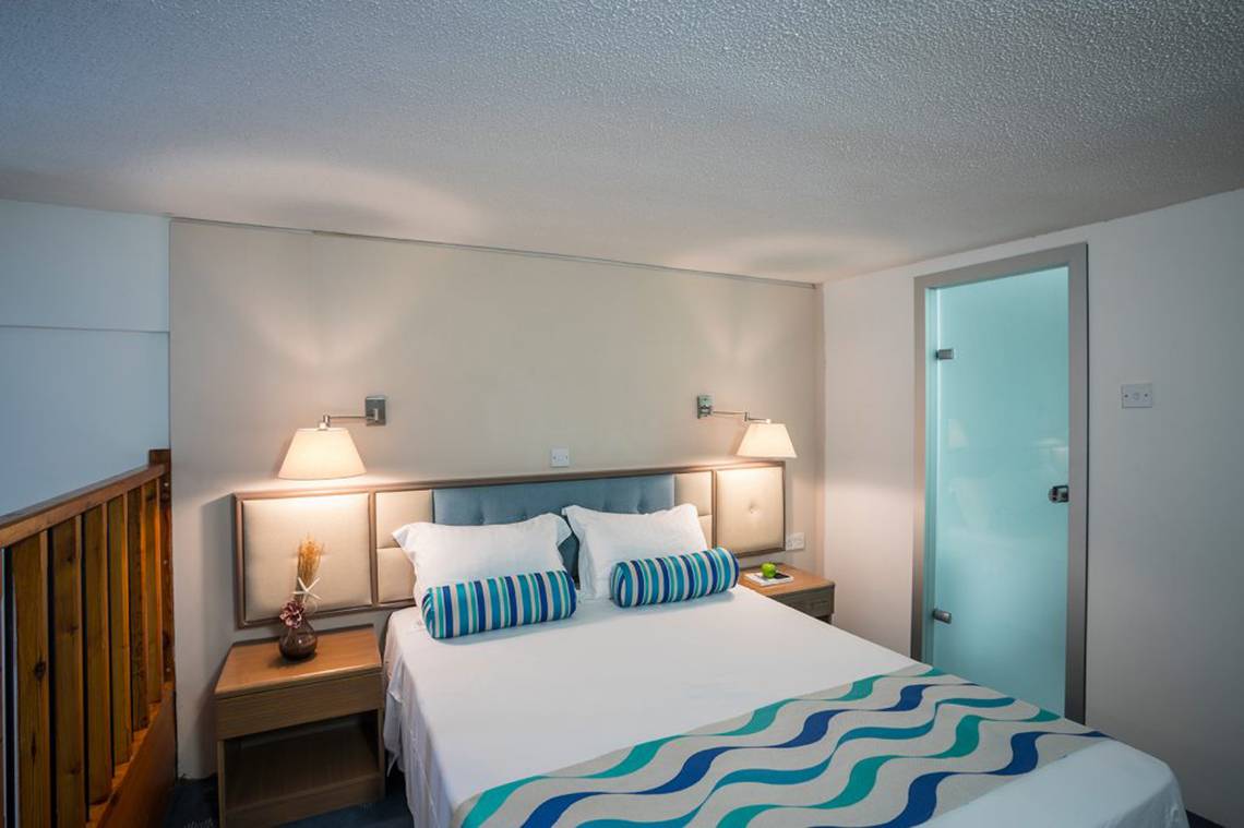 Schlafzimmer im Cavo Maris Beach Hotel mit Bett, Nachttischen und Wandlampen.