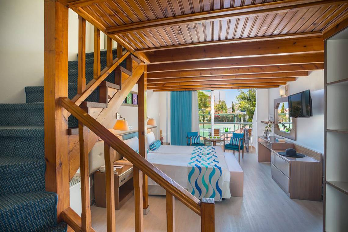 Innenansicht eines Zimmers im Cavo Maris Beach Hotel mit Bett, Stairs, Möbeln und Fernseher.