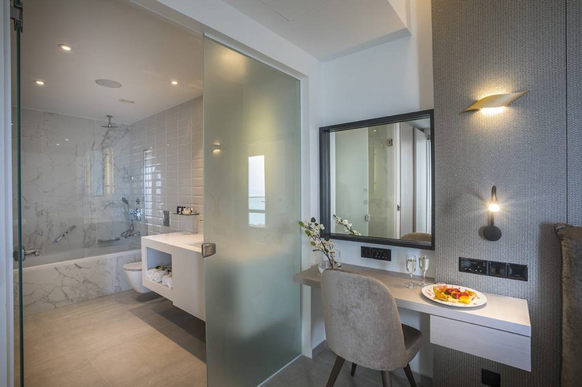 Badezimmer des Cavo Maris Beach Hotels mit Glastür, Badewanne und Schreibtisch.