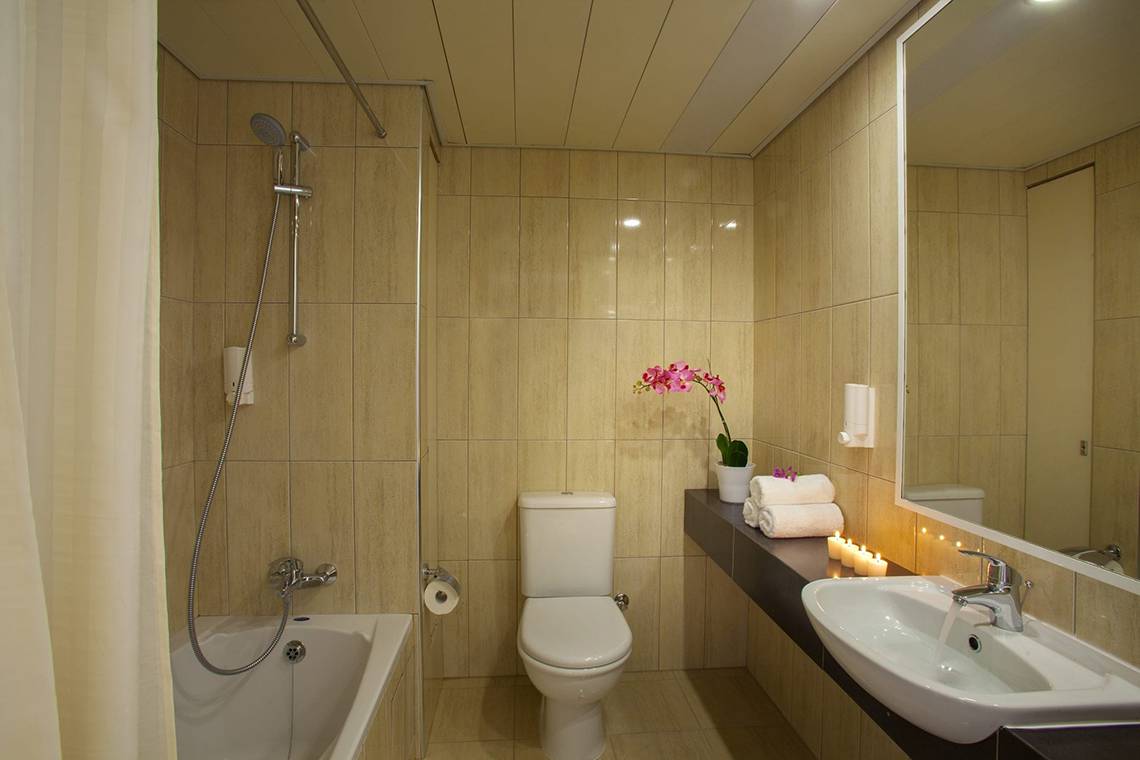 Badezimmer im Queens Bay Hotel mit Badewanne, Toilette, Waschbecken und Spiegel.