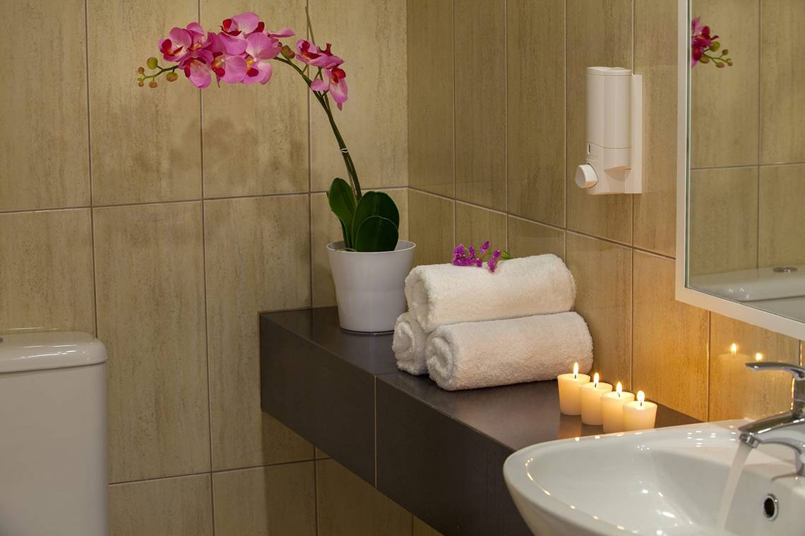 Badezimmer im Queens Bay Hotel mit Blumen, Kerzen und Handtüchern auf der Theke.