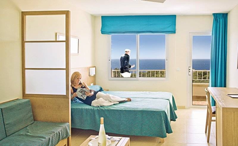 Eine Frau liegt auf einem Bett im Hotelzimmer mit Blick auf das Meer.