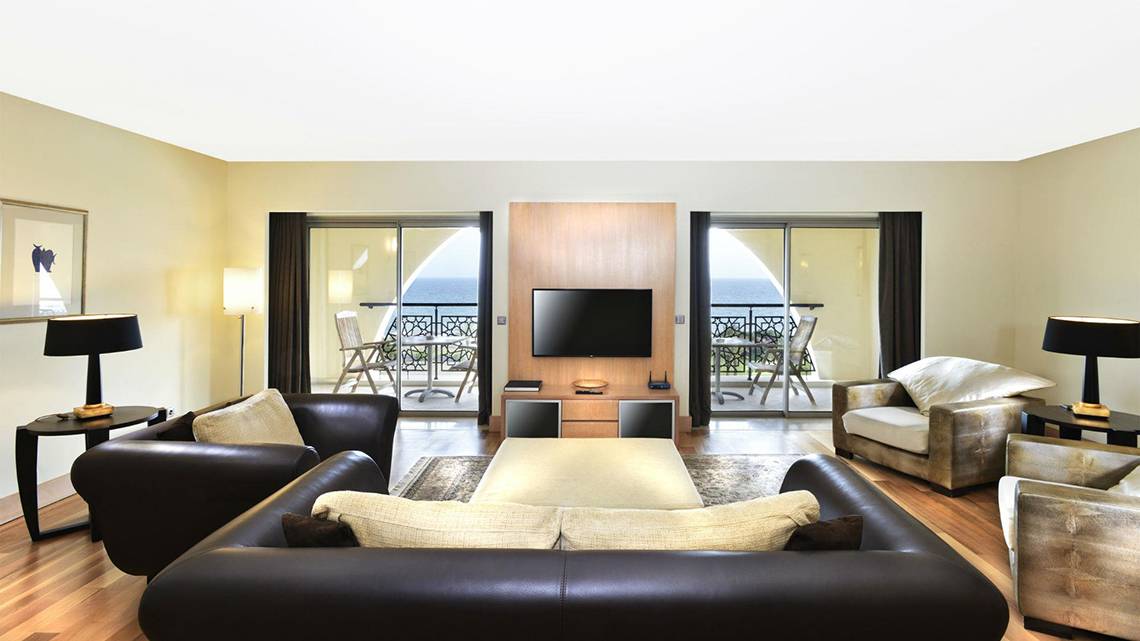 Wohnzimmer im Kempinski Hotel The Dome Belek mit Fernseher, Sofas und Blick aufs Meer.