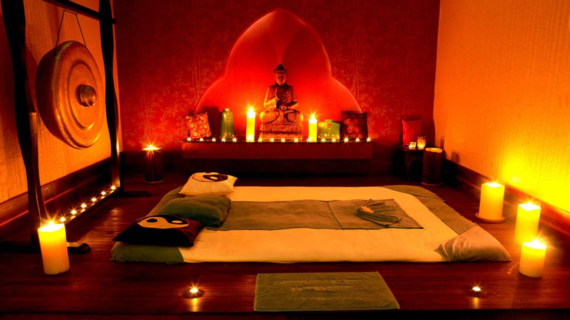 Meditationsraum im Kempinski Hotel The Dome Belek mit roten Wänden, einem Buddha-Standbild, Kerzen und Meditationskissen.