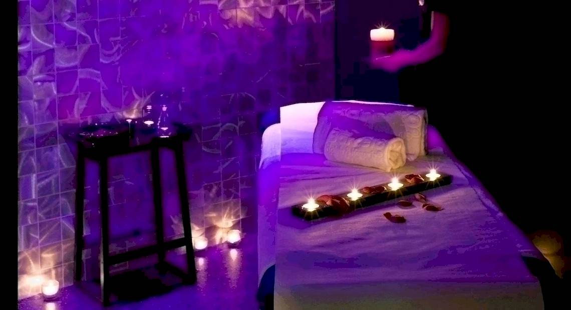 Spa-Behandlungsraum im Barcelo Raval Hotel mit violettem Licht und Kerzen auf einem Tisch.
