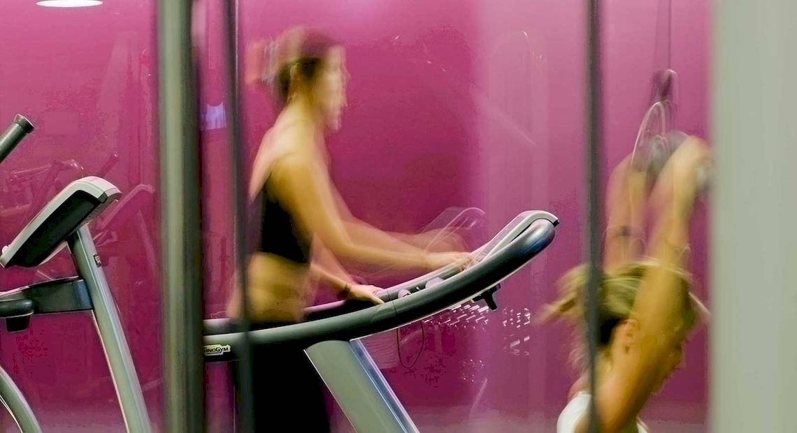 Frau auf dem Laufband im Fitnessstudio mit pinker Wand im Hintergrund