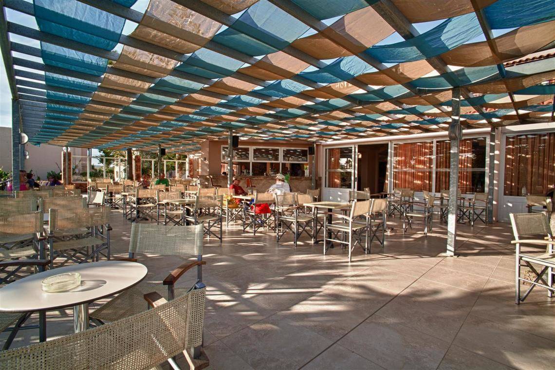Terrasse des Ilios K. Village Resorts mit schattenspendenden Überdachungen und Tischen.
