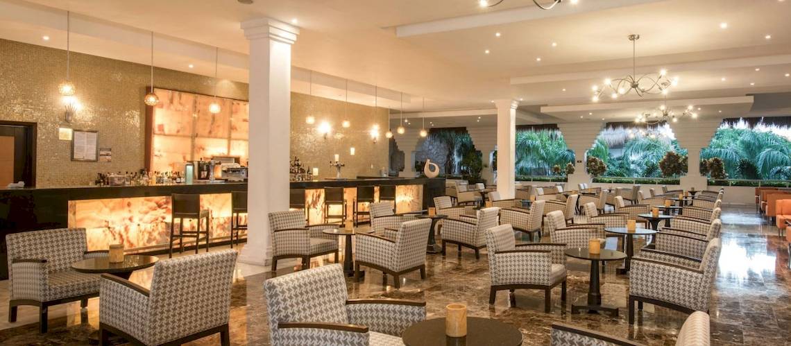 Die Lobby des Grand Riviera Princess Hotels mit Bar, Stühlen und Tischen.