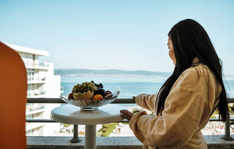 Frau auf Balkon mit Meerblick im Festa Panorama Hotel, Obstschale auf Tisch