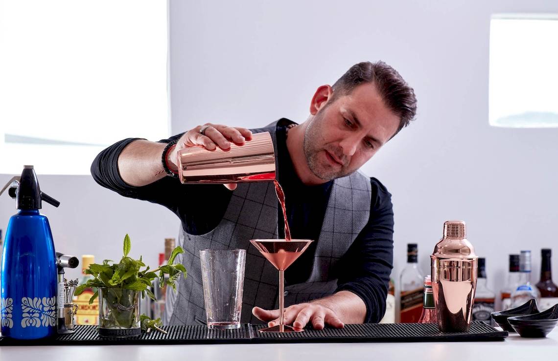 Ein Mann, der ein Glas mit einer silbernen Cocktailmischung füllt, steht an einer Bar.