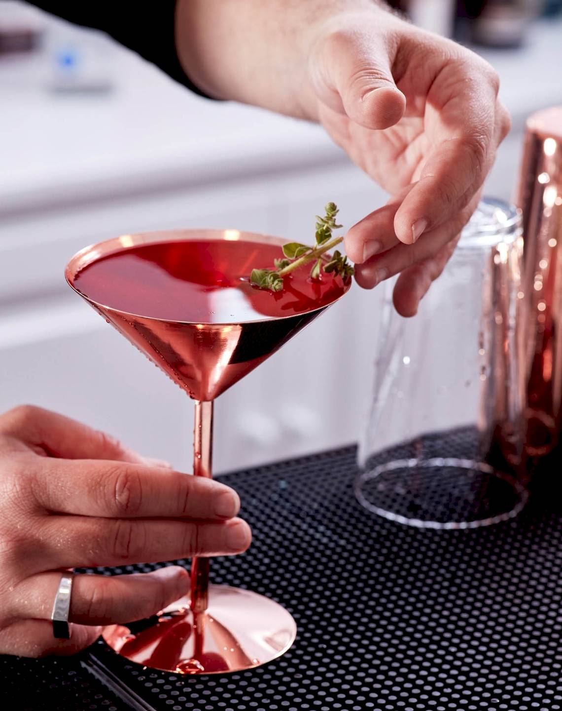Barkeeper gibt einen Cocktail mit Thymian einhändig in ein Glas.