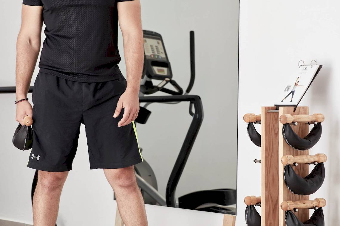 Mann im Trainingsraum vor einem Laufband und Spiegel, der ein Hantelgewicht in der Hand hält.