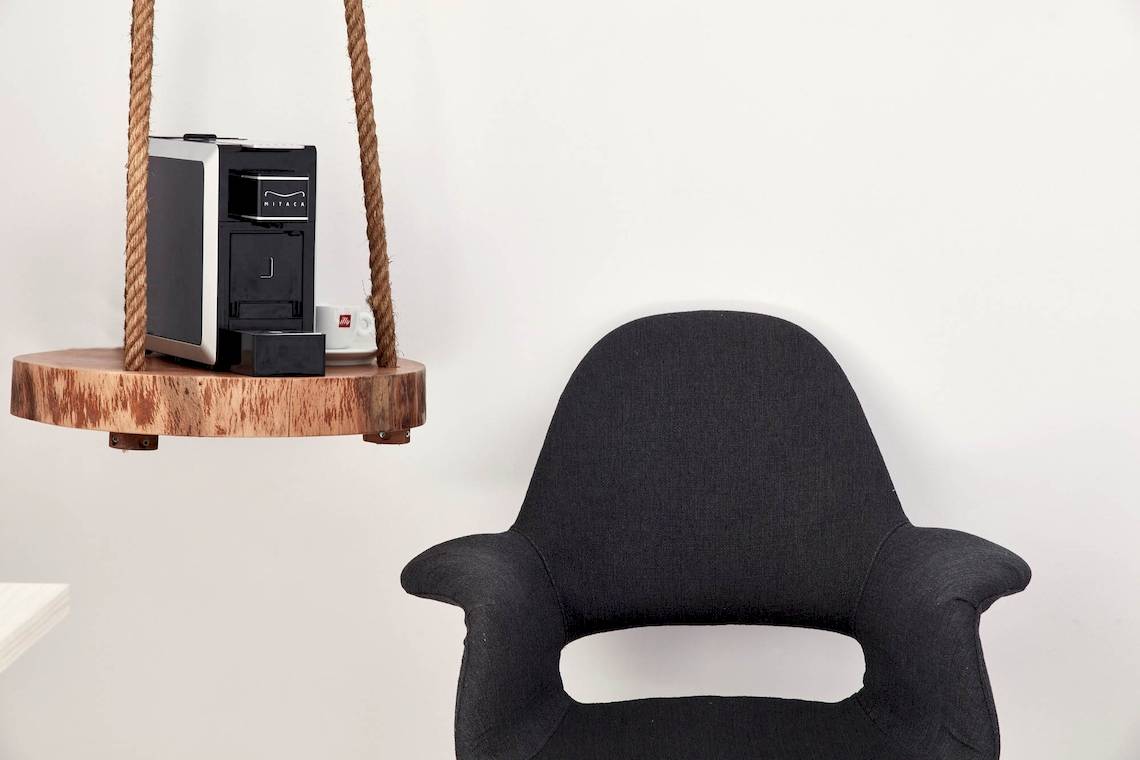 Schwarzes Sofa neben einer Holzplatte mit Kaffeemaschine und Geschirr.