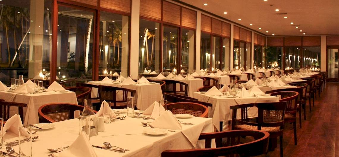Ein elegantes Restaurant im Blue Water Hotel und Spa mit gedeckten Tischen und Stühlen, großen Fenstern und Blick auf die Außenbeleuchtung.